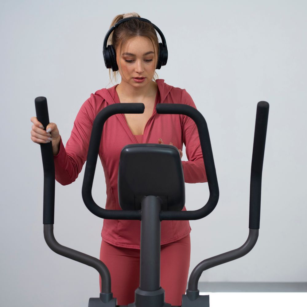 Woman exercising on a cross trainer with headphones on a plain background